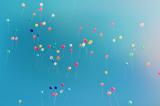 Dozens of small, brightly coloured balloons drifting upward against a clear blue sky.